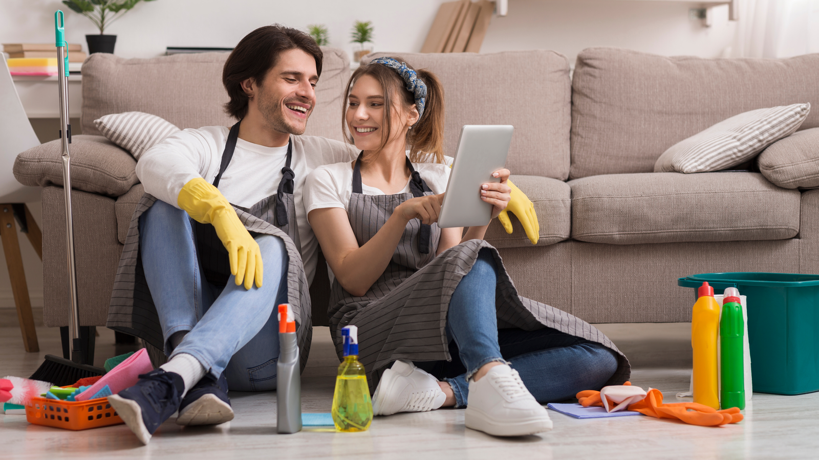 Cheerful young couple pausing from cleaning to use an app on a tablet