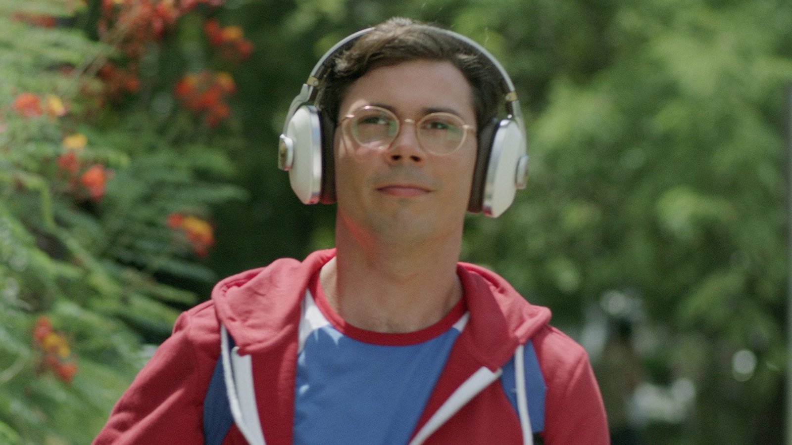 A man wearing a hoodie and headphones walks down a street.